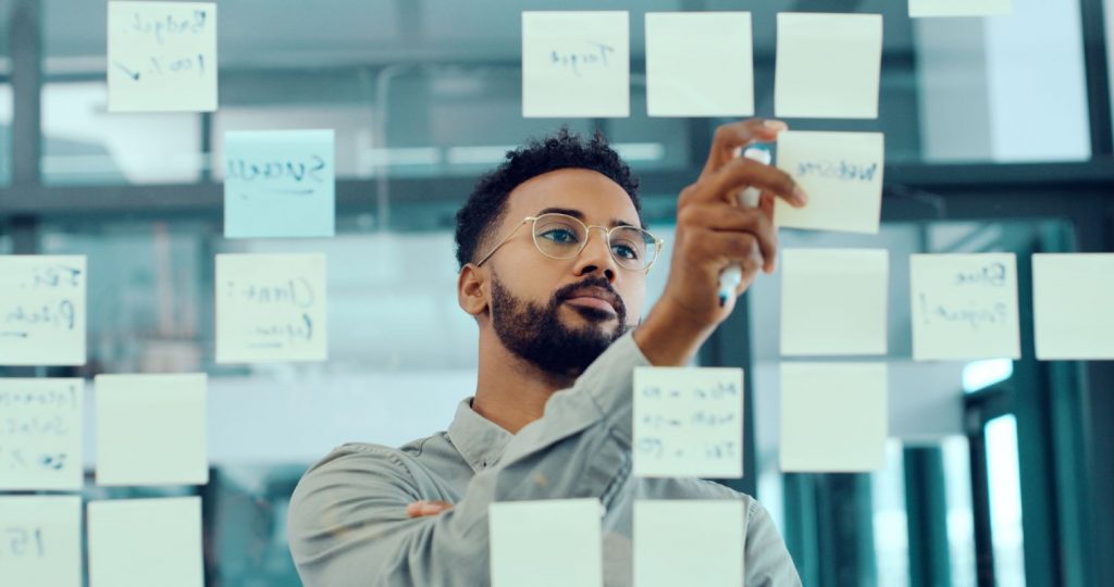 Man working through sticky note exercise on clear panel