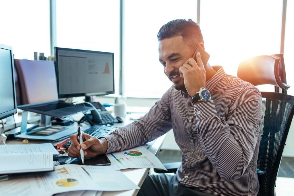 Man talking on phone while looking at printed statistics 